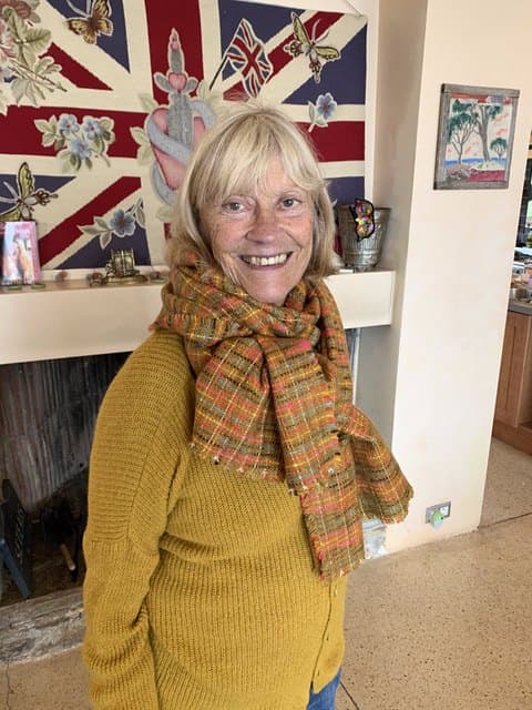 Kate’s mother smiling over her shoulder in a mustard cardigan and a tweed scarf, at home